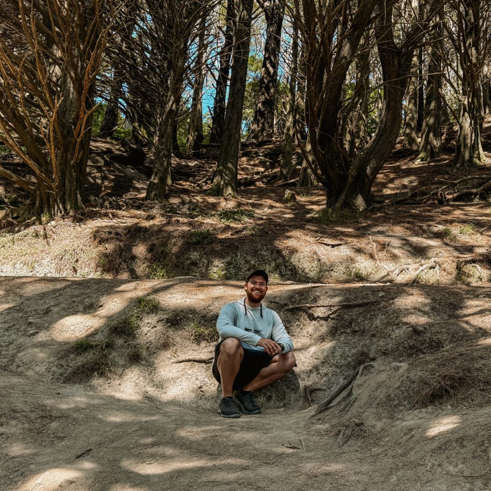 New Zealand-North Island-Wellington-25 A man crouching on the ground with a forest behind him in Wellington