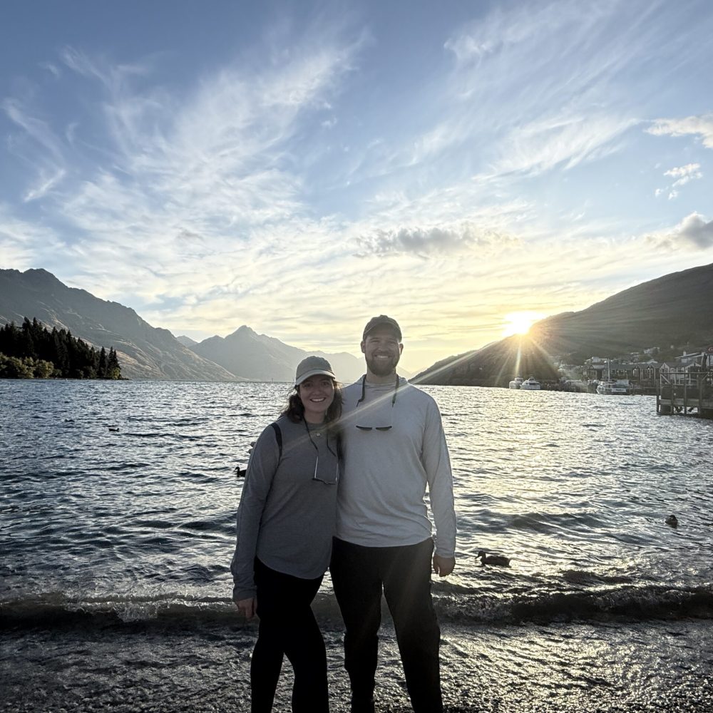 New Zealand-Queenstown-7 Two people standing in front of a lake as the sun is setting when visiting Queenstown