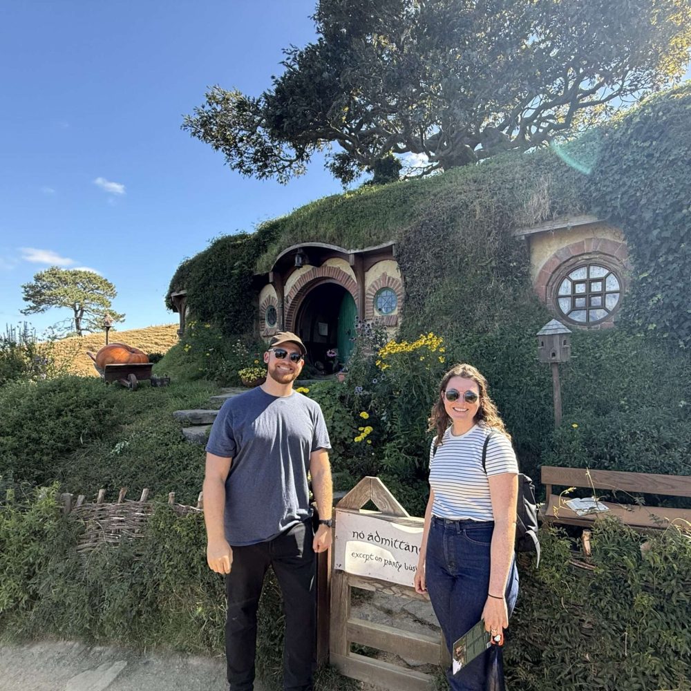 Two people standing in front of a small home built into a hill