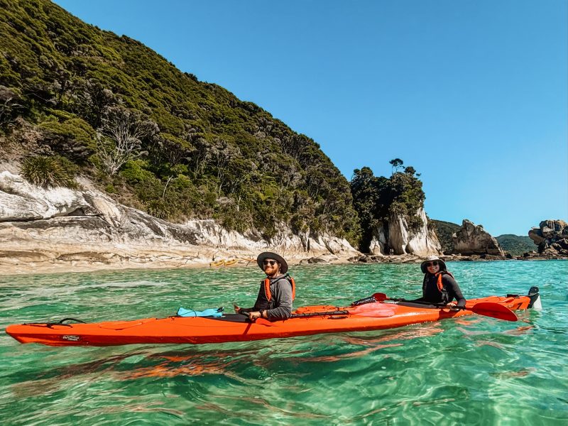 Two people in a kayak in turquoise water with a coastline behind them in Abel Tasman National Park