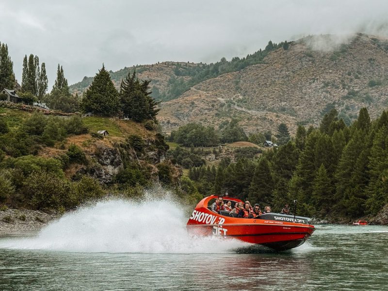 A boat splashing through a river between mountains that can be done on a Queenstown itinerary and one of the top things to do in New Zealand