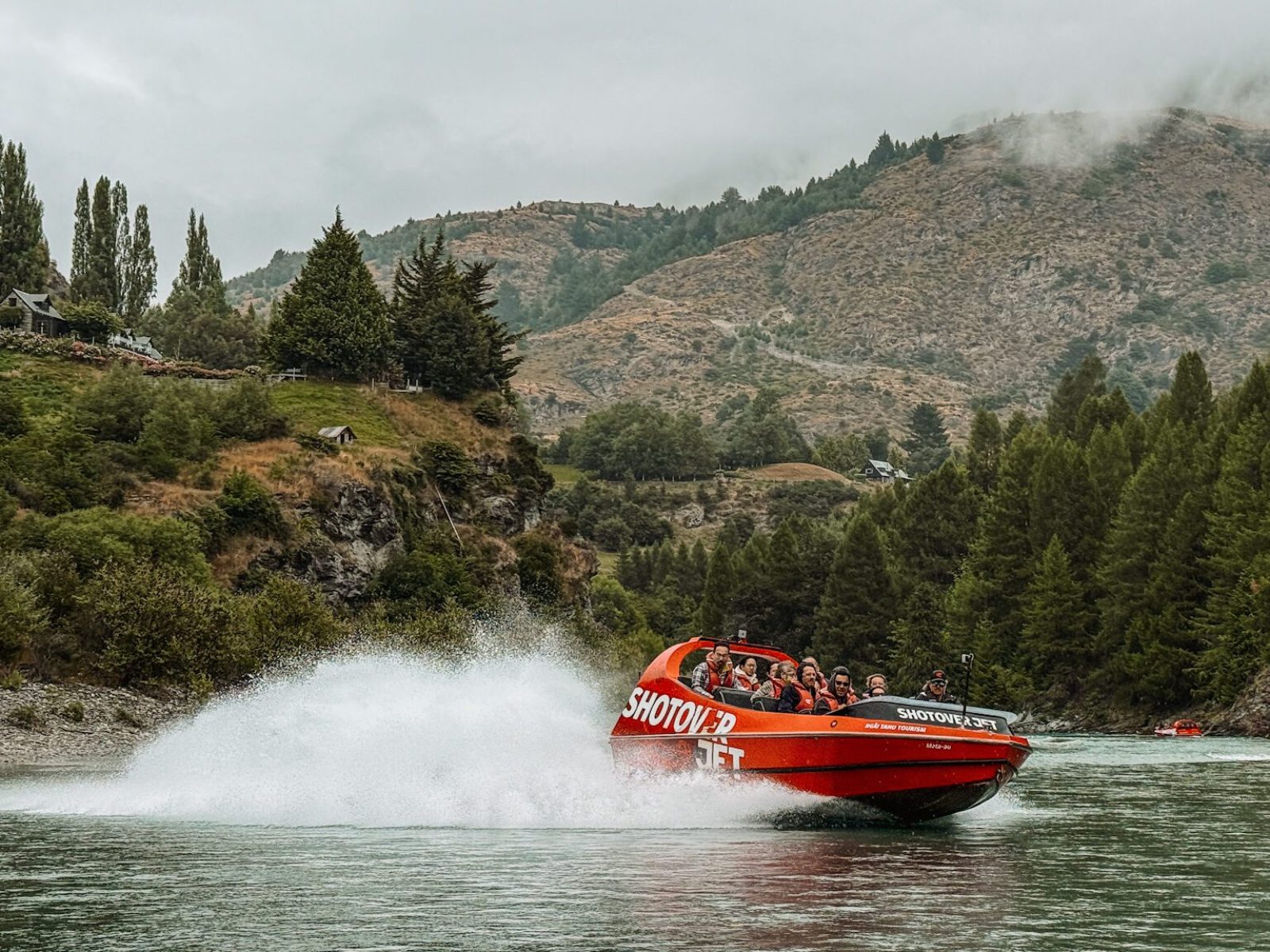 New Zealand-South Island-Queenstown-25 A boat splashing through a river between mountains that can be done on a Queenstown itinerary and one of the top things to do in New Zealand
