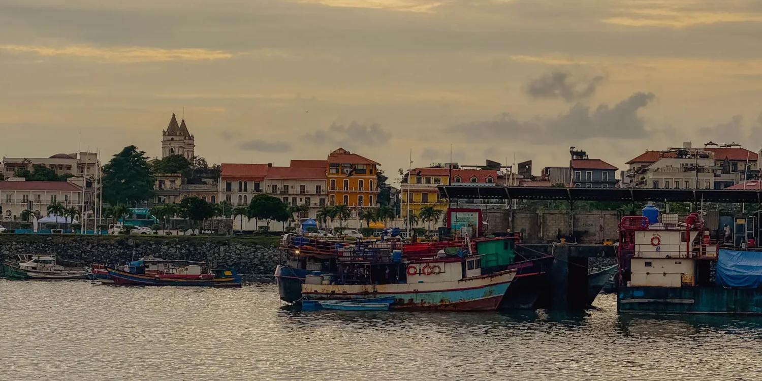 Fishing boats moored in front of the Casco Viejo waterfront at dusk, with colonial buildings and a church tower visible behind — Panama City travel guide