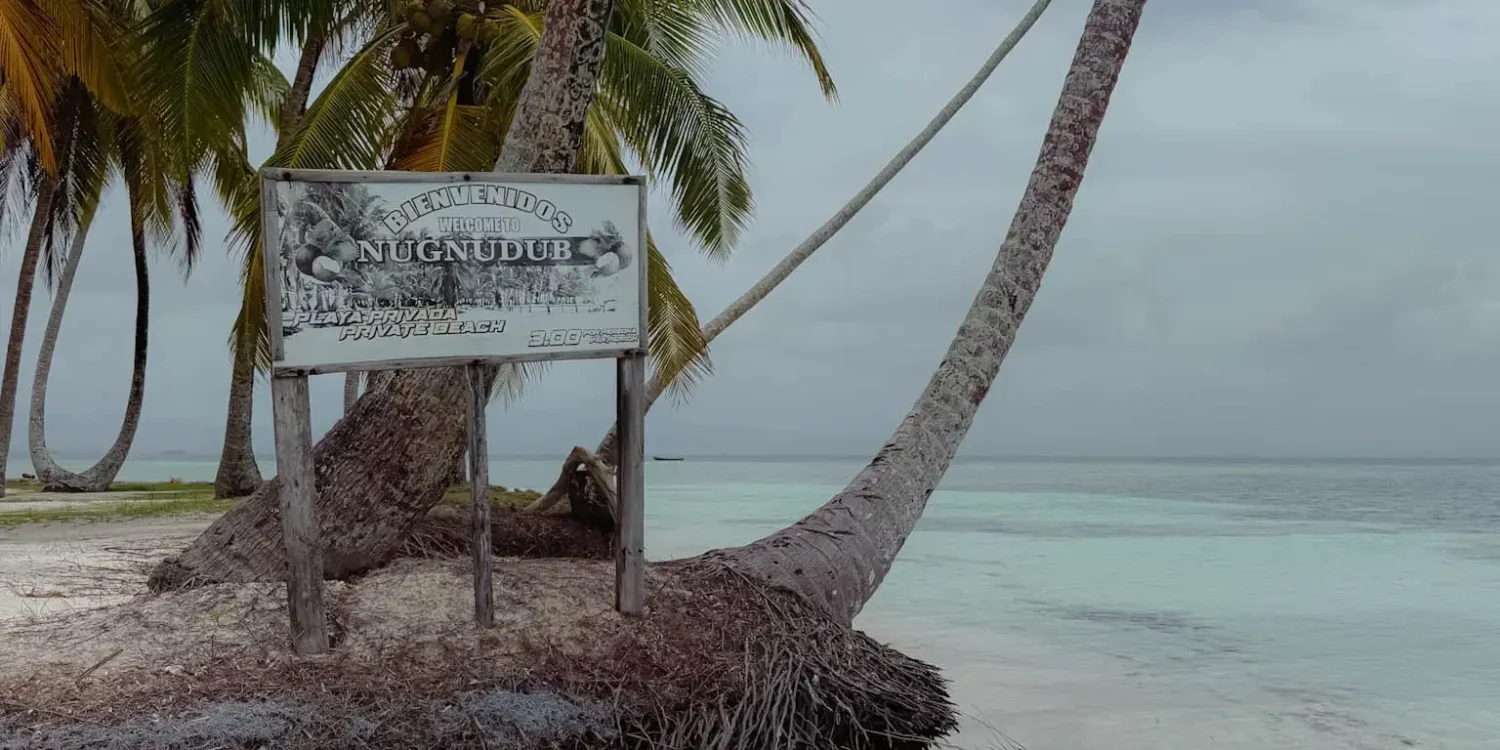Leaning palm trees and a Nugnudub island welcome sign on the white sand beach in San Blas - San Blas Islands Guna Yala