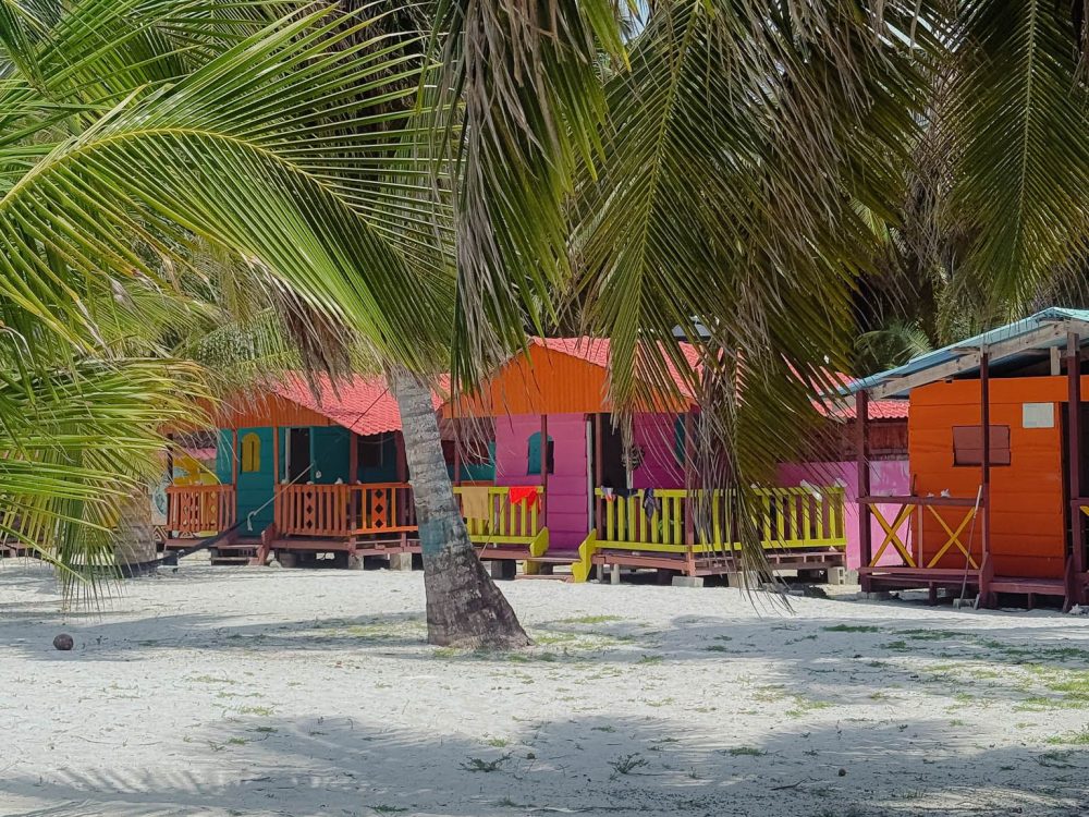 Colorful painted wooden island cabins on stilts under palm trees on a San Blas island - island accommodation San Blas Guna Yala