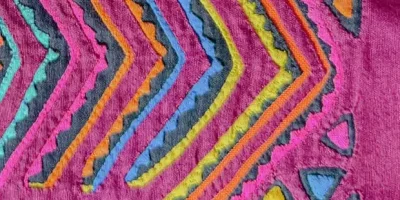 Close-up of a traditional Guna mola textile showing intricate reverse-appliqué geometric patterns in red pink and orange - Guna Yala Panama