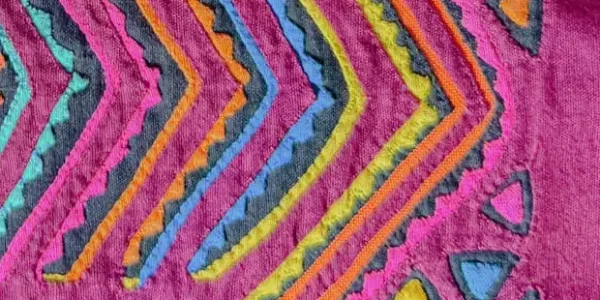 Close-up of a traditional Guna mola textile showing intricate reverse-appliqué geometric patterns in red pink and orange - Guna Yala Panama