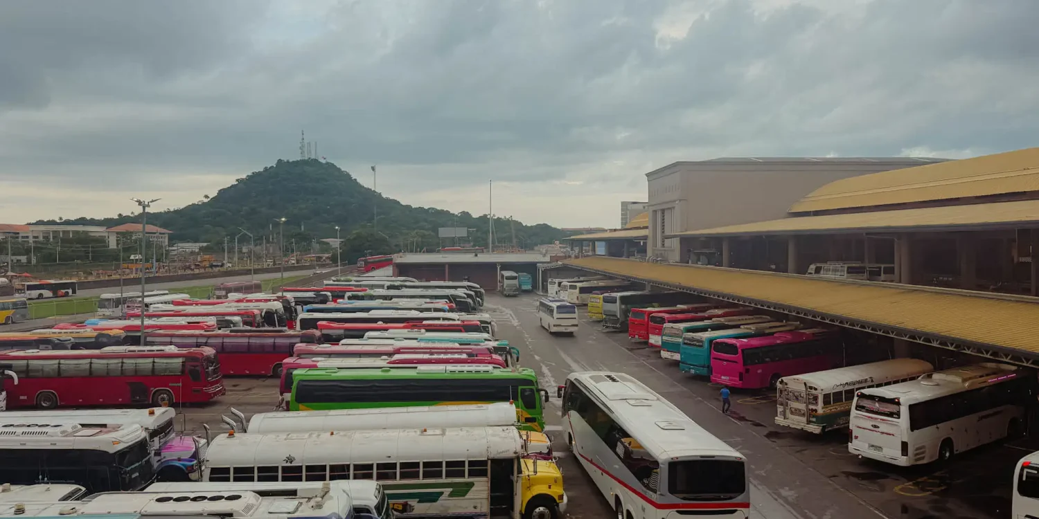 Colorful buses packed into Albrook Bus Terminal in Panama City with a green hill in the background -- Boquete Panama