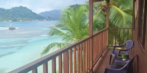 Wooden balcony at Cabanas Blue with two chairs overlooking turquoise water and palms on Isla Grande -- Portobelo Panama