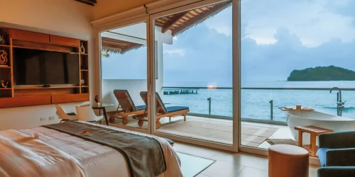 Interior of an overwater bungalow at Ordovician Beach Resort with floor-to-ceiling glass doors opening to the Caribbean sea at dusk -- Portobelo Panama