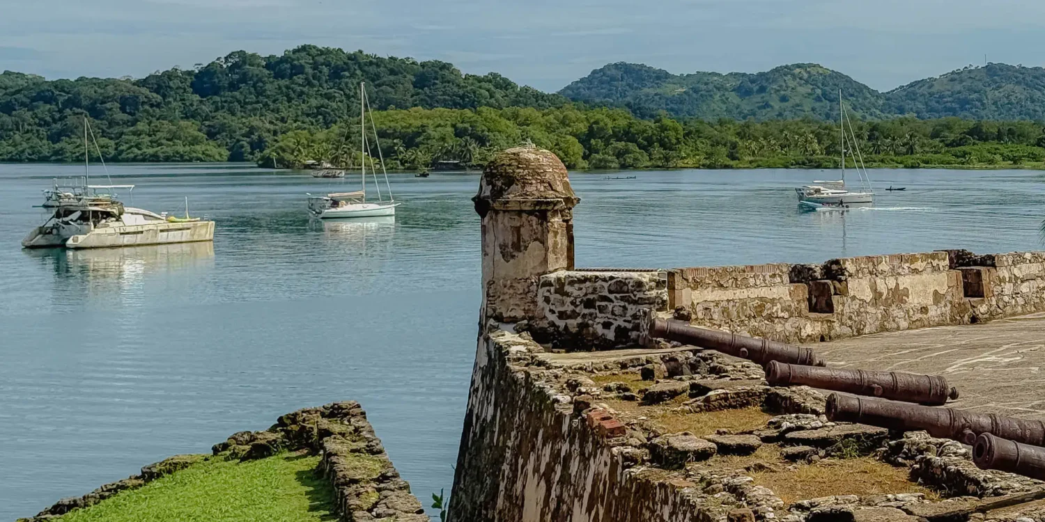 portobelo-fort-sentry-tower-cannons-bay-sailboats Stone sentry tower and cannons on a Portobelo fort wall with sailboats on the bay and jungle hills behind -- Portobelo Panama