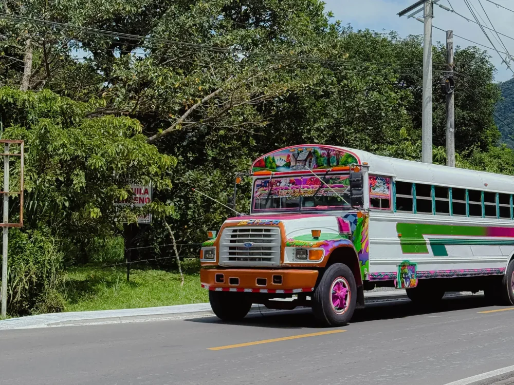 A brightly painted Panamanian diablo rojo bus on the road to Valle de Anton surrounded by tropical vegetation -- Valle de Anton Panama